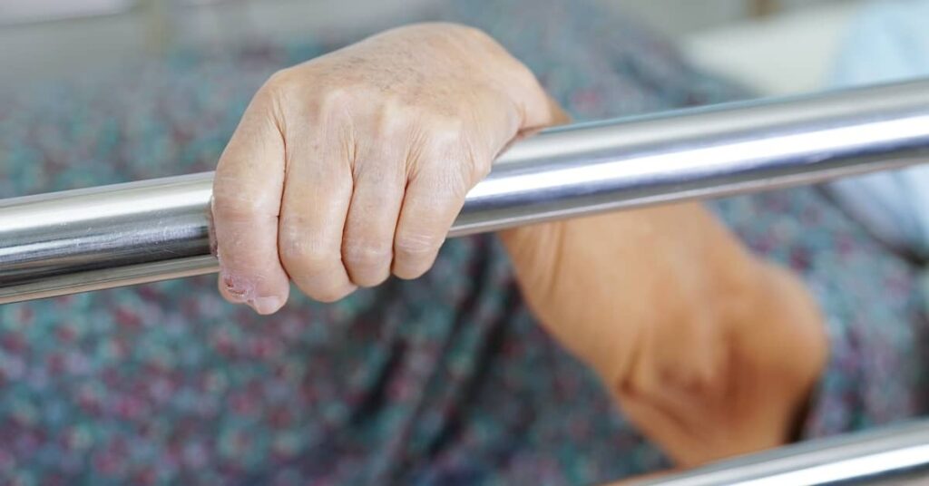 Neglected senior woman holding onto the bed rail in nursing home | Burg Simpson