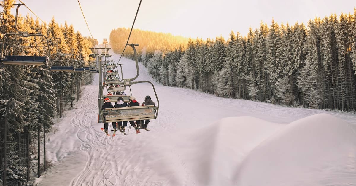 Skiers riding a chairlift up the slope at a ski resort | Burg Simpson